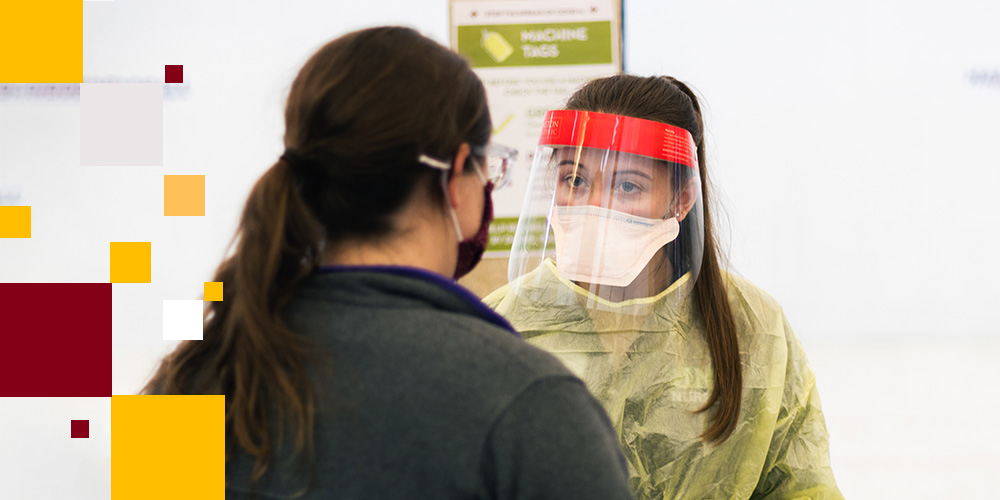 Healthcare provider in PPE talking with a patient wearing a mask
