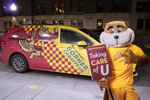 Goldy stands in front of a Gopher Chauffeur van holding a sign that says 'Taking Care of U'