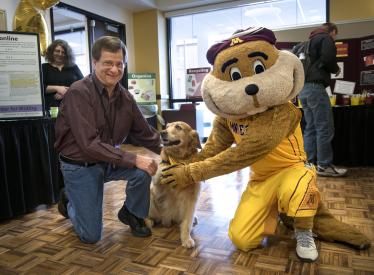 Goldy the gopher pets a dog with a friend